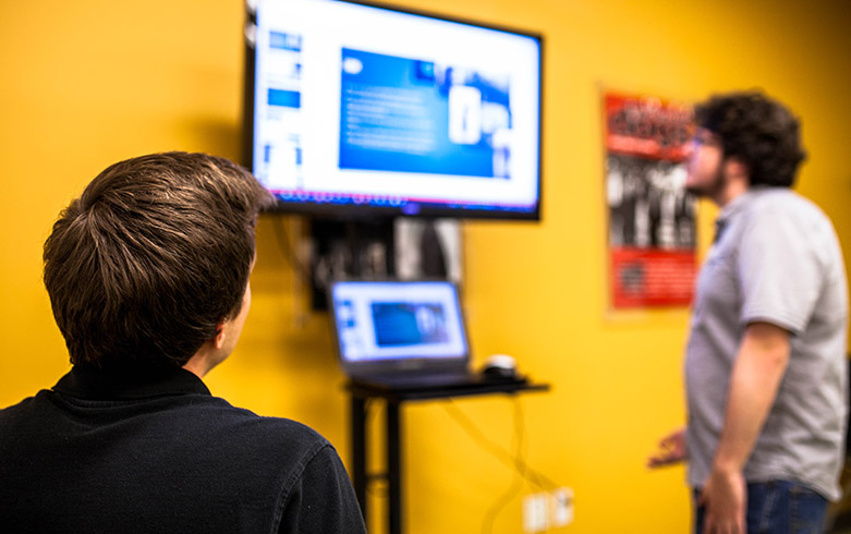 2 male students viewing a powerpoint presentation on a large monitor