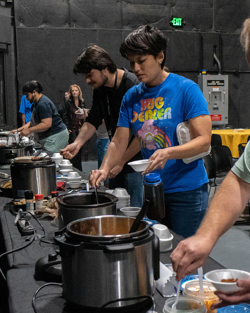 UCF Downtown staff and students serve themselves chili in crockpots lined up along long tables with black tablecloths in the CMB Soundstage