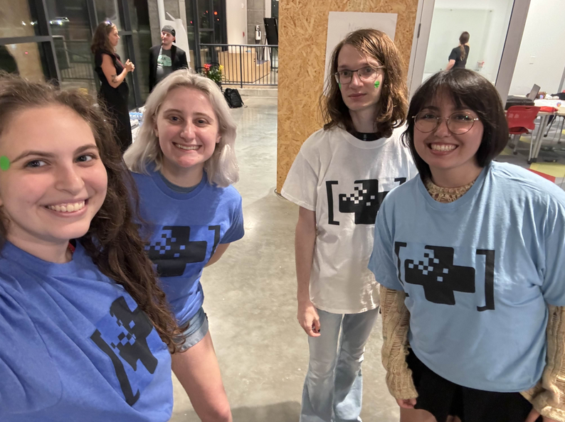 Four FIEAns from cohorts 20 and 21 stand facing the camera, selfie style, with their white and blue MeGa Health Jam tees on.