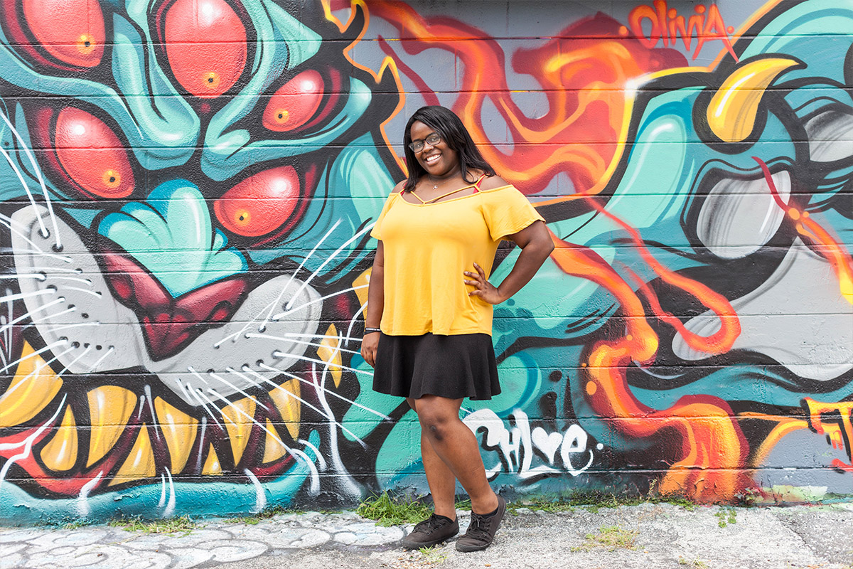 Female student posing outside infront of graffiti filled wall