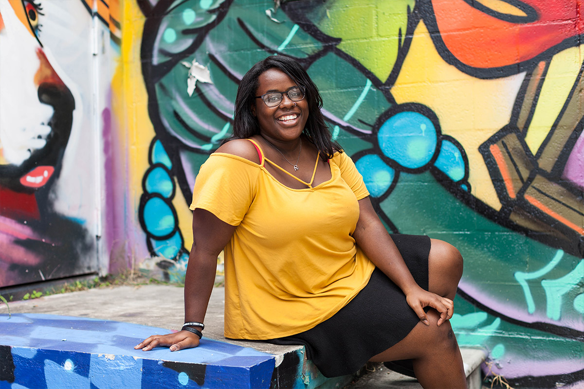 Female student posing outside infront of graffiti filled wall