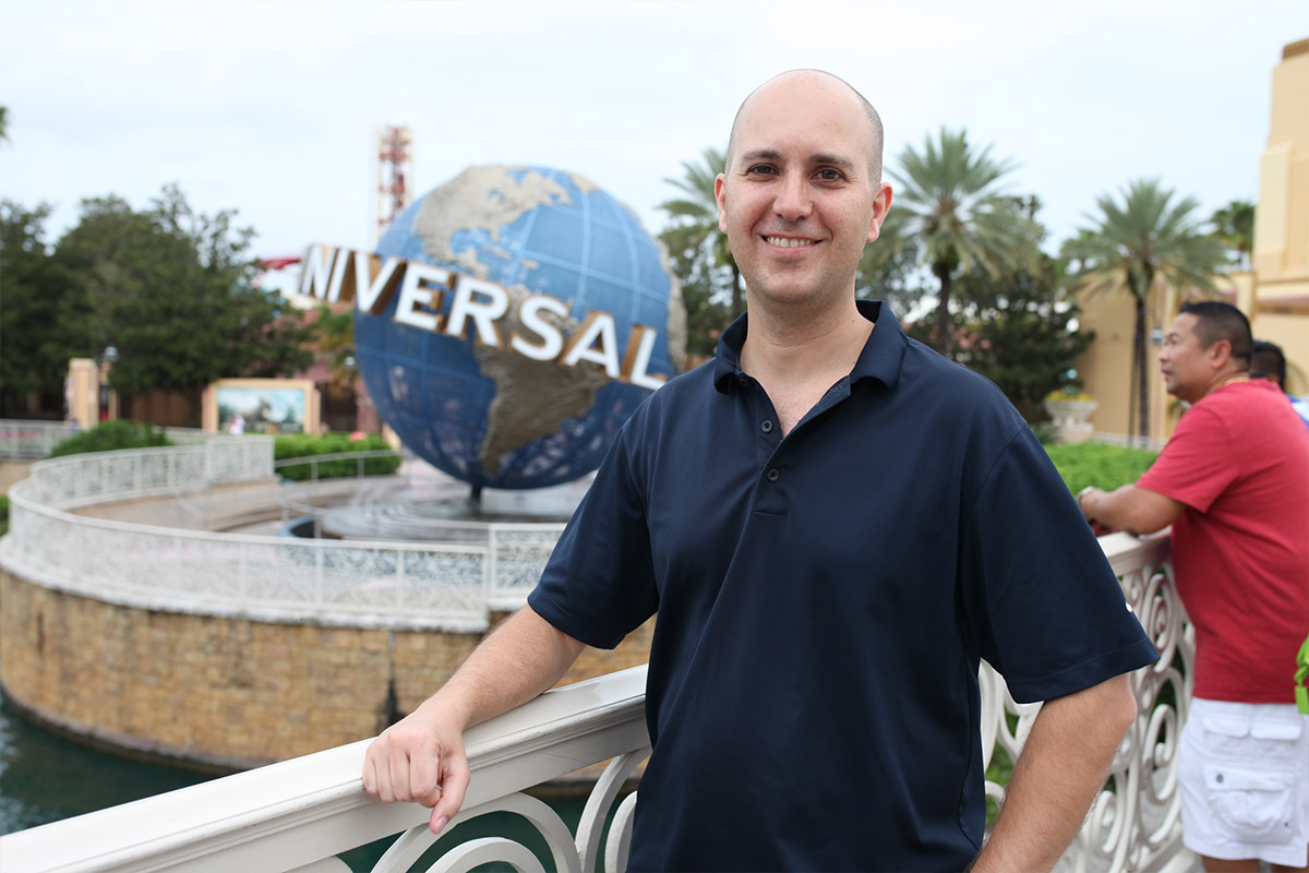 Male student standing outside of Universal globe sign