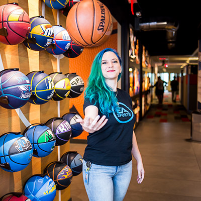 Female alumni with bright green hair juggling a basketball standing infront of NBA live basketball wall