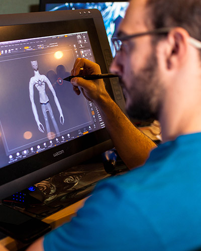 Young male student drawing on a 3D character large wacom display