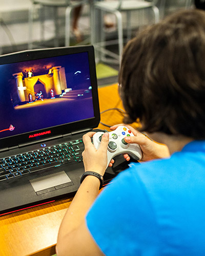 Young female student playing videogames on a laptop computer with a controller