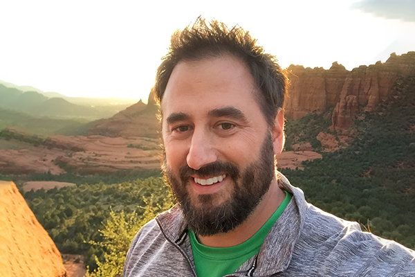 Headshot of Jeremy Paulding, man with brown spiky hair and beard with Arizona landscape background