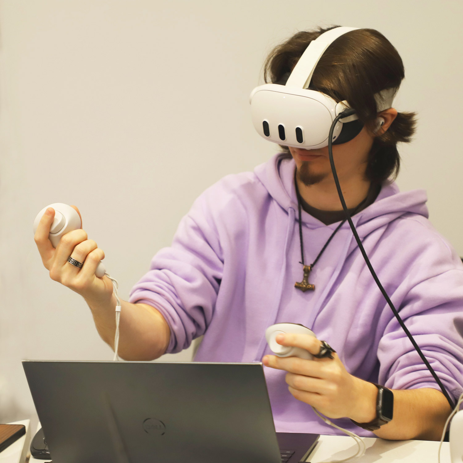 A student in a purple hoodie playtests his VR game with a VR headset on sitting at a table.